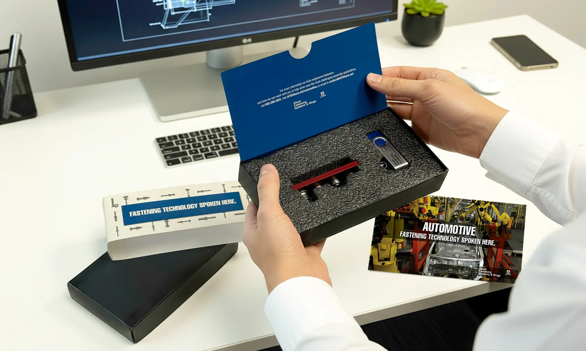 Hands opening a branded fastening technology sample kit at an office desk.