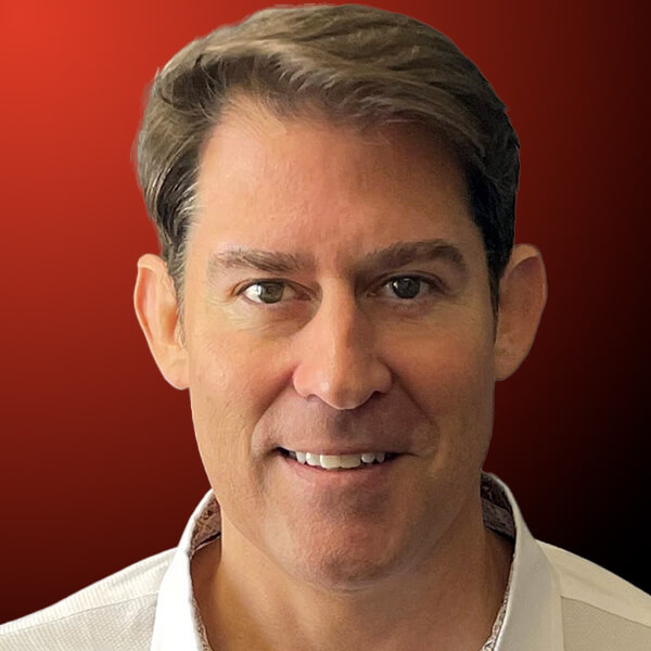 Professional headshot of a man with short hair wearing a white shirt against an orange to black gradient background.