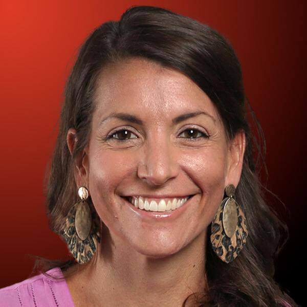 Professional headshot of a smiling woman with dark hair against an orange to black gradient background.