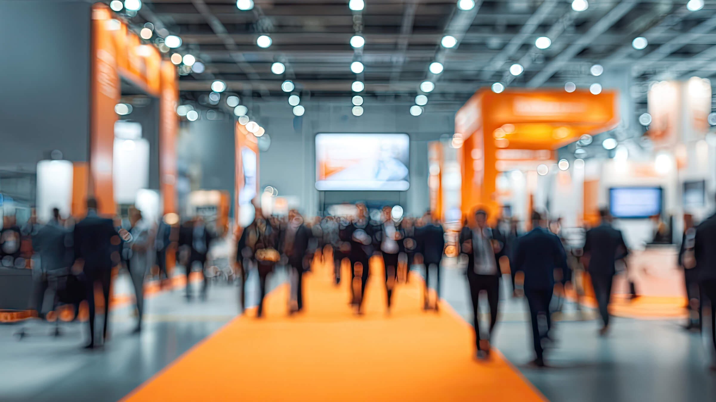 Blurred crowd walking through modern trade show floor with orange booths, creative event planning and exhibition marketing.