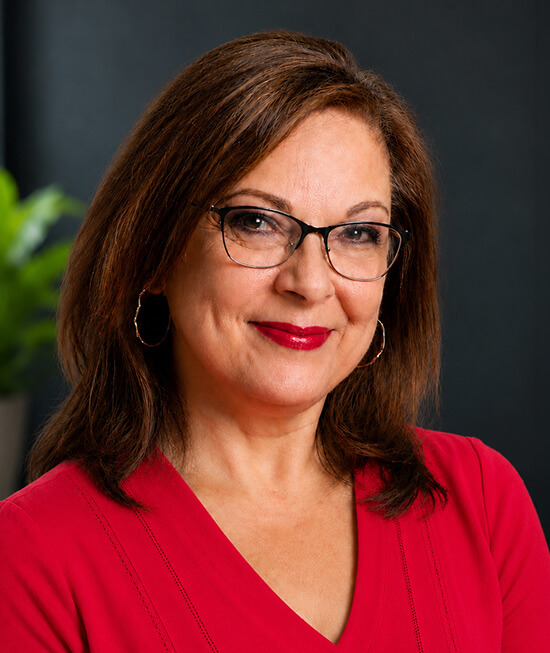 Professional headshot of a smiling woman with brown hair, wearing a red shirt.