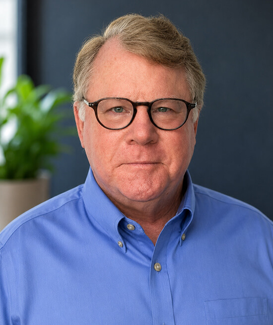 Professional headshot of a man wearing a blue shirt and glasses with short light hair.