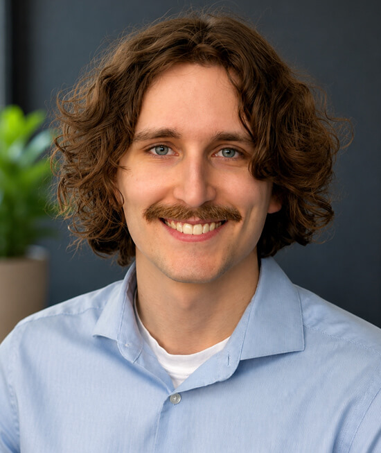 Professional headshot of a smiling man with wavy hair wearing a blue shirt.